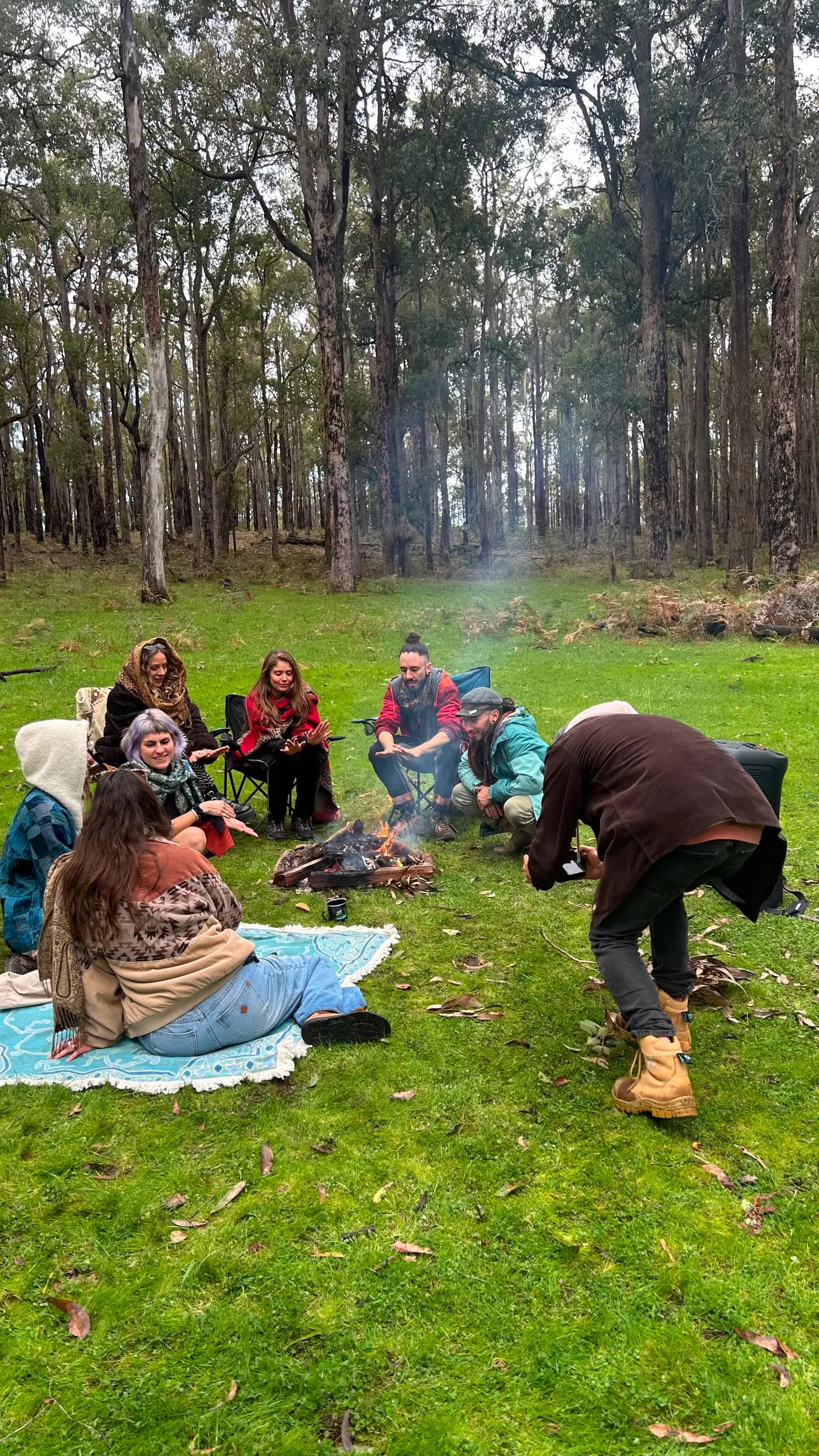 A group of people gathering around a small fire in a forest clearing